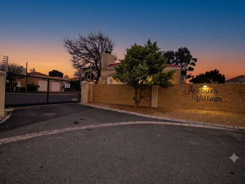 Entrance view of Avebury Village featuring a brick boundary wall, secure electric gate access, and paved driveway at dusk.