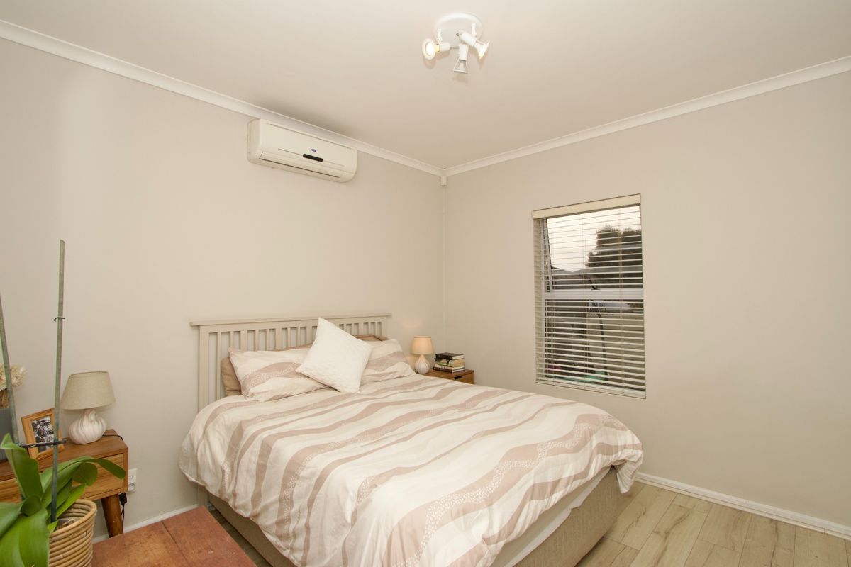 A well-maintained bedroom featuring neutral walls, laminate flooring, a wall-mounted split-system air conditioner, and venetian blinds for privacy.
