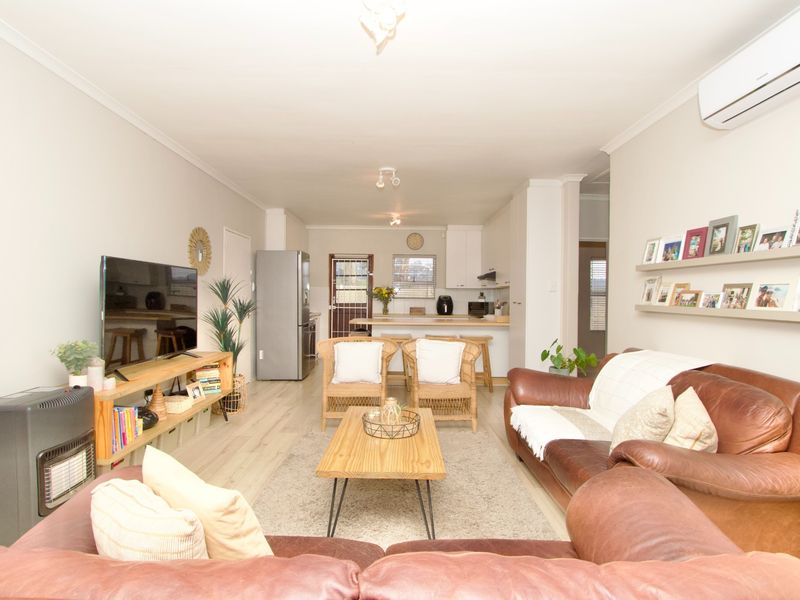An open-plan living and kitchen area featuring laminate flooring, a split-system air conditioner, and a functional kitchen layout with a breakfast bar.
