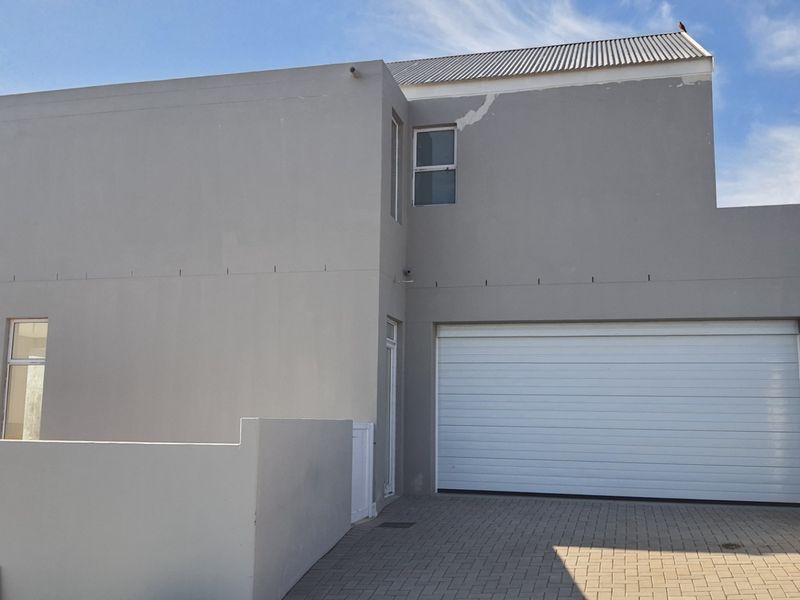 Front exterior view of the property featuring a double garage, paved driveway, and modern plastered facade with visible maintenance requirements.