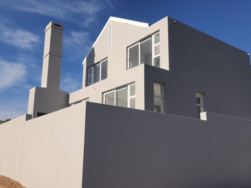 Rear view of a modern double-storey house featuring a prominent chimney, clean rendered facade, and secure boundary walling.