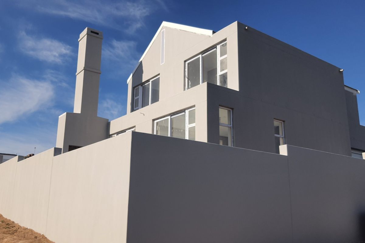Rear view of a modern double-storey house featuring a prominent chimney, clean rendered facade, and secure boundary walling.