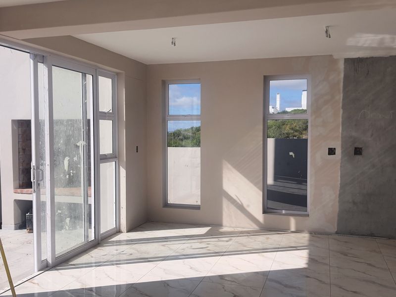 An empty living area featuring large sliding doors, tiled floors, and an adjacent outdoor braai area, currently undergoing finishing work on the walls.