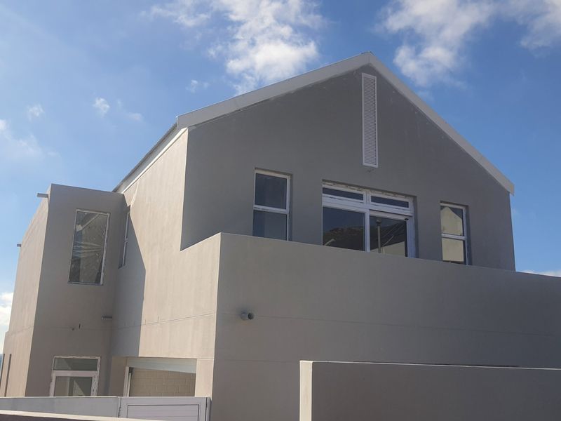 Rear elevation of a modern double-story house featuring a balcony, clean rendered facade, and views of the surrounding area.