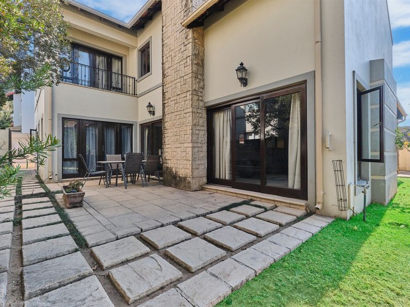 Rear exterior view featuring a paved patio area, stone-clad chimney, and sliding glass doors leading into the home.