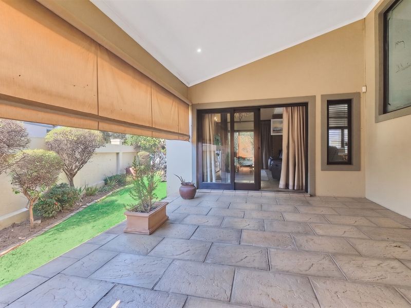 A covered patio area featuring tiled flooring, a retractable outdoor blind, and sliding glass door access to the interior living space.