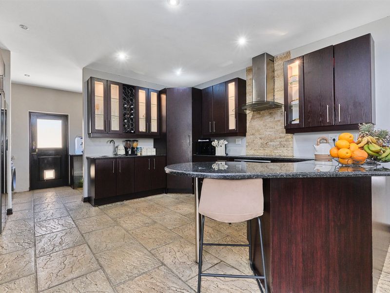 Modern kitchen featuring dark wood cabinetry, granite countertops, a central island, and stone tile flooring, complemented by integrated lighting and a stainless steel extractor.