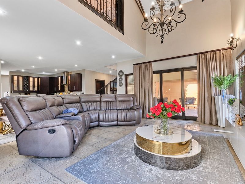 Spacious open-plan living area featuring high vaulted ceilings, stone tile flooring, and seamless flow to the outdoor patio through large sliding glass doors.