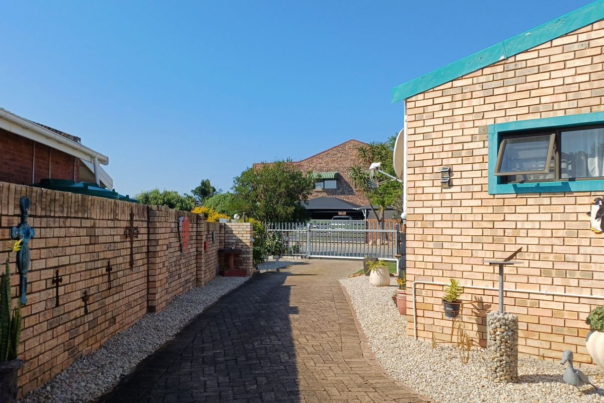 A paved driveway leading to a metal security gate, flanked by face brick walls and low-maintenance pebble landscaping.