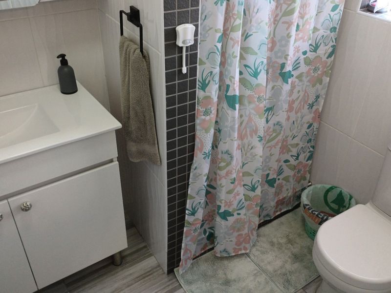 A functional bathroom featuring a modern white vanity with a basin, a toilet, and a shower area with a mosaic tiled feature wall.