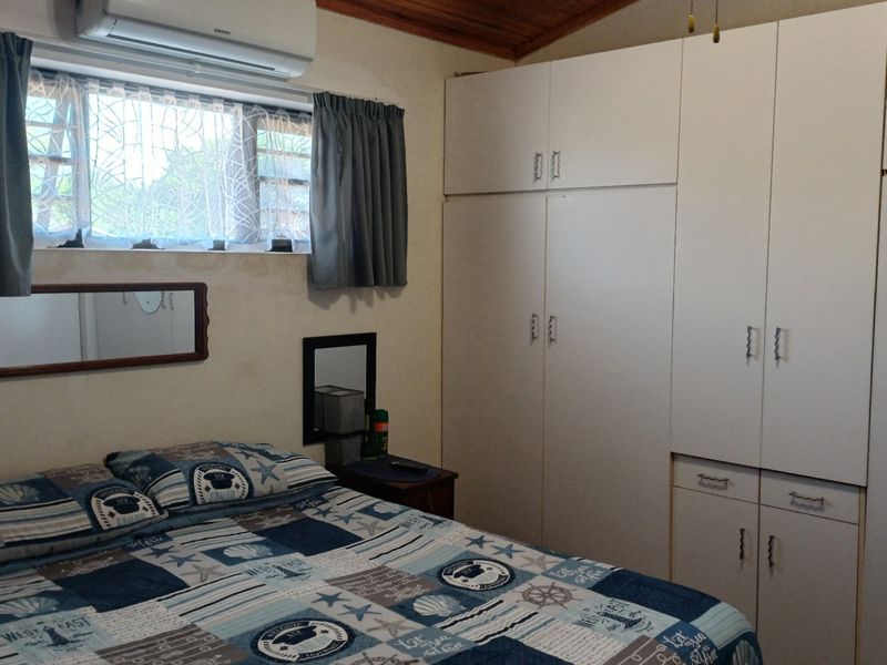 A bedroom featuring built-in cupboards, a timber ceiling, and an air conditioning unit, with security bars installed on the window.