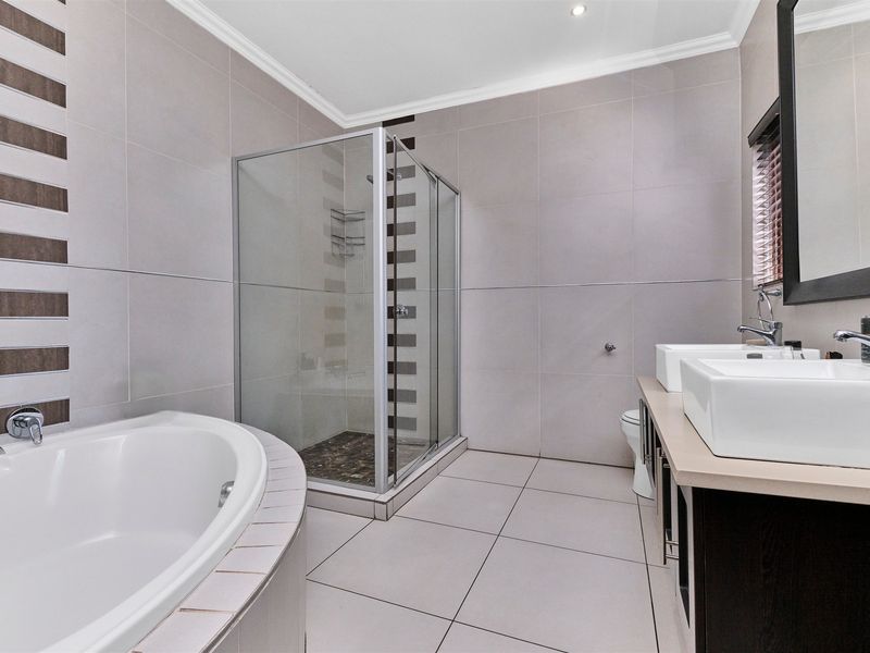 Modern bathroom featuring a built-in bathtub, separate glass shower enclosure, and a double vanity with contemporary fixtures and neutral tiling.