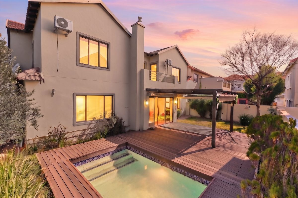 Rear exterior view featuring a swimming pool, timber decking, and a pergola, set against a well-maintained residential facade with sliding door access.