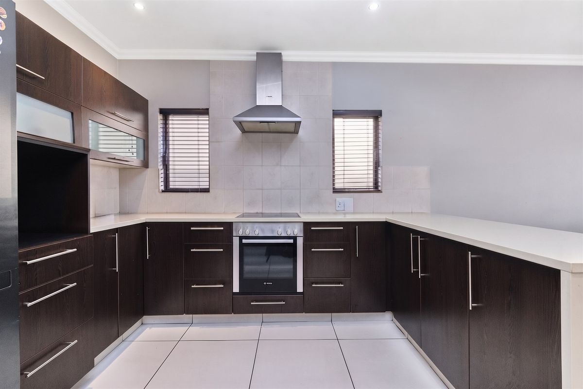 Modern kitchen featuring dark wood cabinetry, stone countertops, stainless steel oven, extractor fan, and tiled flooring in a clean, well-maintained space.