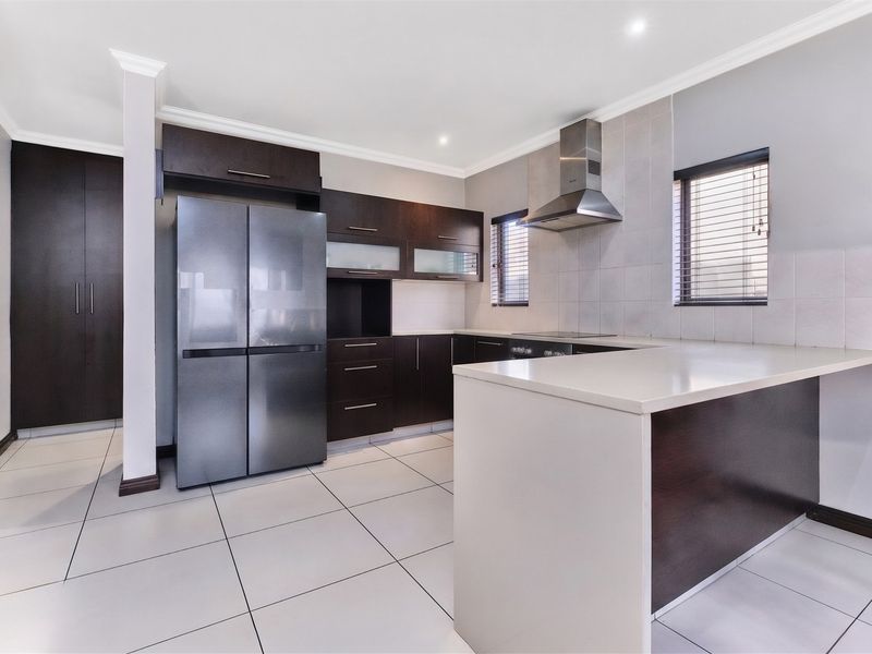 Modern kitchen featuring dark wood cabinetry, stone countertops, stainless steel extractor fan, and neutral ceramic floor tiles in a clean, open layout.