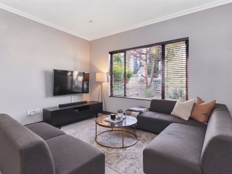 A well-maintained living room featuring neutral walls, tiled flooring, recessed lighting, and a large window with venetian blinds providing natural light.