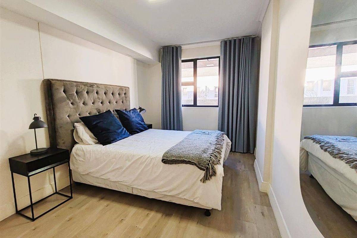 A well-maintained bedroom featuring light-toned laminate flooring, neutral walls, and a window with floor-to-ceiling curtains.