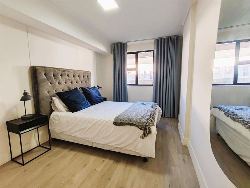 A well-maintained bedroom featuring light-toned laminate flooring, neutral walls, and a window with floor-to-ceiling curtains.