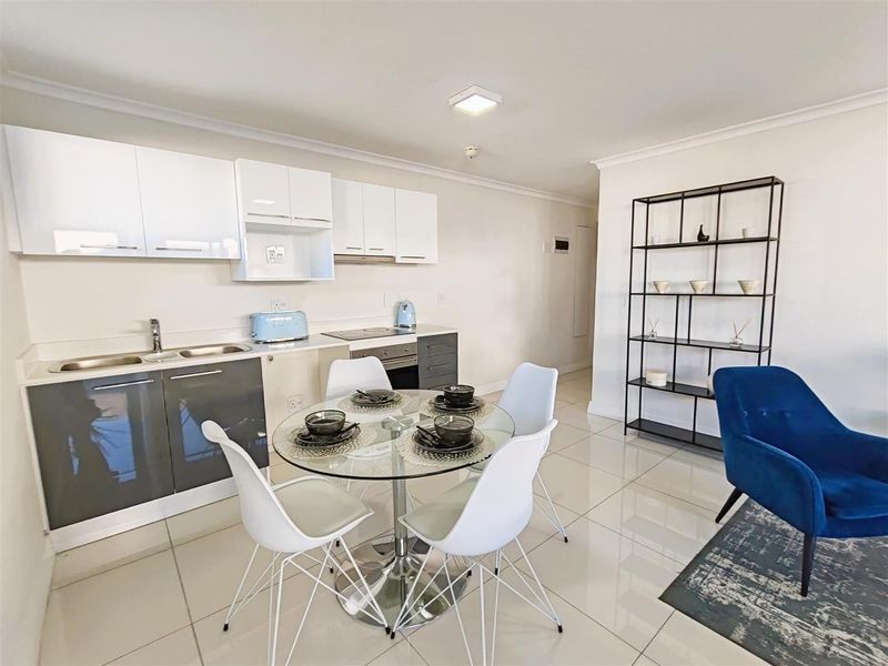 Modern open-plan apartment featuring a sleek kitchen with built-in cabinetry, integrated appliances, and polished tiled flooring throughout the living and dining area.