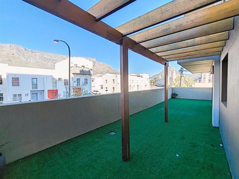 Spacious balcony featuring a timber pergola structure, concrete balustrade, and artificial turf flooring with mountain views.