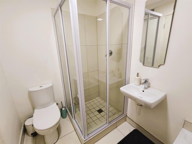 Compact bathroom featuring a corner shower enclosure, wall-mounted basin, and toilet with neutral floor and wall tiling.