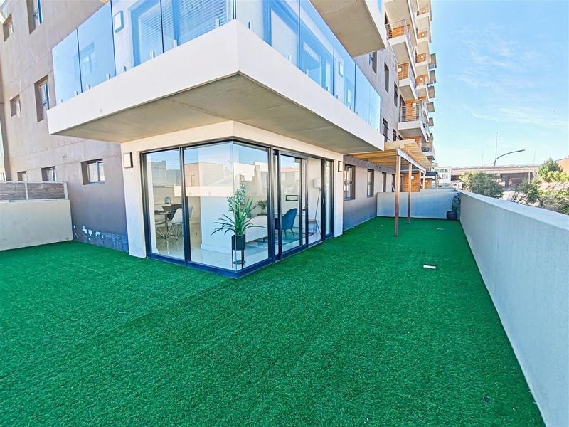 Spacious apartment balcony featuring artificial turf, a timber pergola, and modern glass balustrades with direct access to the interior living area.