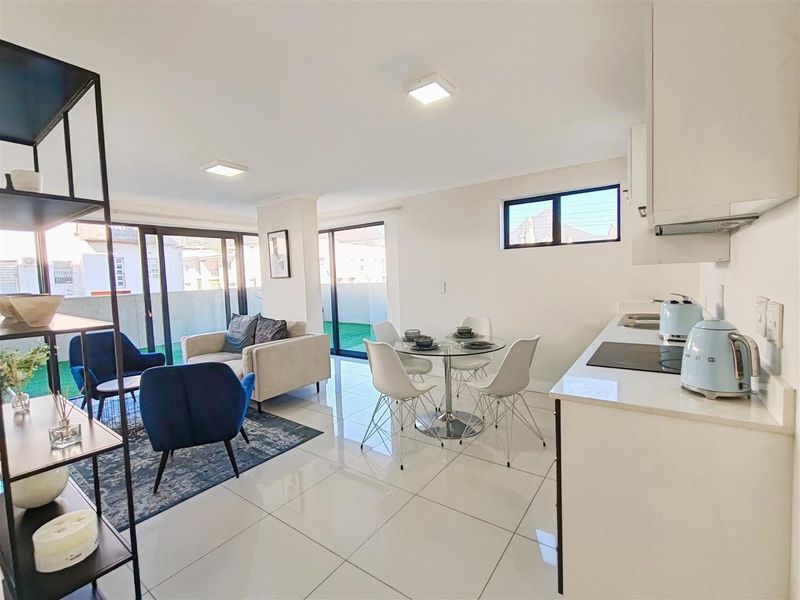 Modern open-plan living area featuring a sleek kitchen with stone countertops, tiled floors, and large sliding doors leading to an outdoor balcony space.