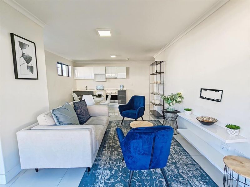 A bright open-plan living and kitchen area featuring modern cabinetry, built-in appliances, tiled flooring, and a functional layout suitable for contemporary apartment living.