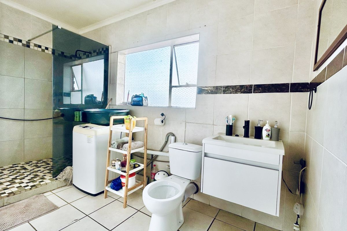 A functional bathroom featuring a walk-in shower with glass screen, wall-mounted vanity, and tiled finishes throughout.