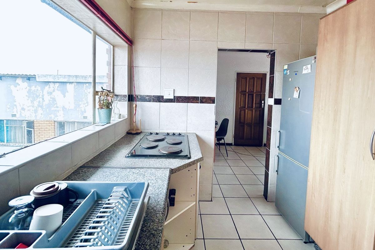A functional kitchen featuring tiled splashbacks, a built-in hob, and tiled flooring, offering a practical layout with potential for cosmetic updates.