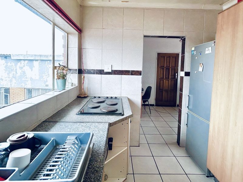 A functional kitchen featuring tiled splashbacks, a built-in hob, and tiled flooring, offering a practical layout with potential for cosmetic updates.