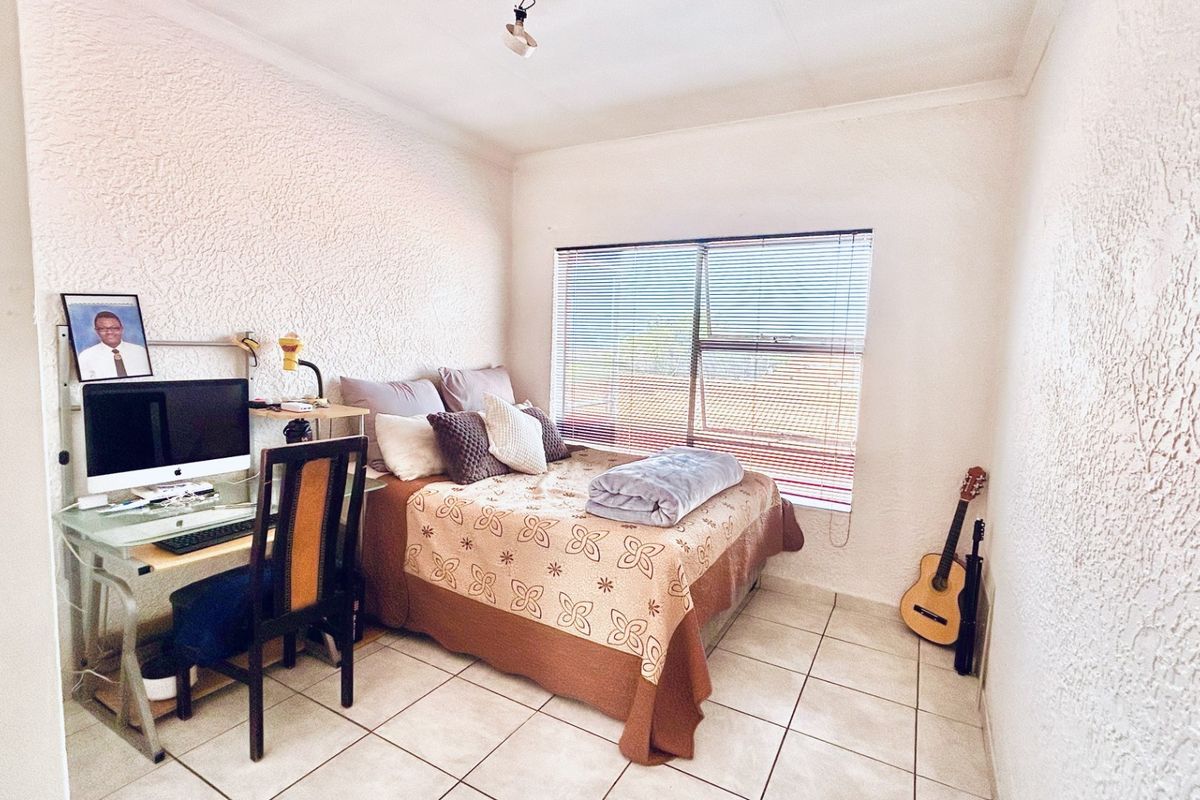 A functional bedroom featuring tiled flooring, textured wall finishes, and a window fitted with venetian blinds.
