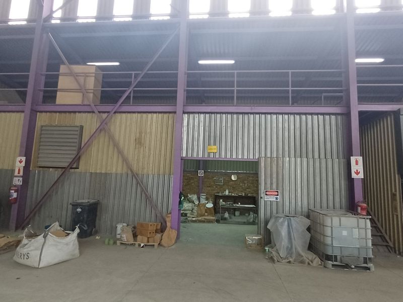 Large industrial utility space featuring high ceilings, a mezzanine level, corrugated metal wall cladding, and concrete flooring suitable for storage or manufacturing operations.