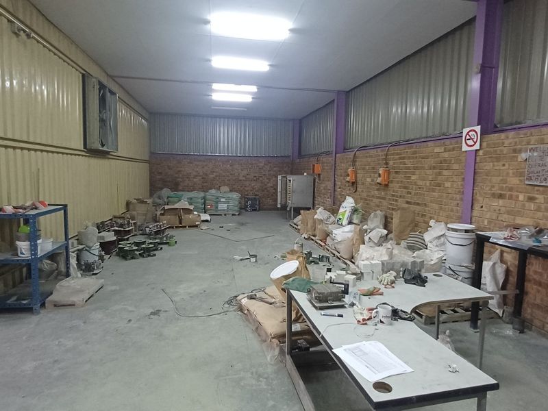 An industrial utility space featuring concrete flooring, exposed brick walls, corrugated metal cladding, and overhead fluorescent lighting, suitable for workshop or storage use.