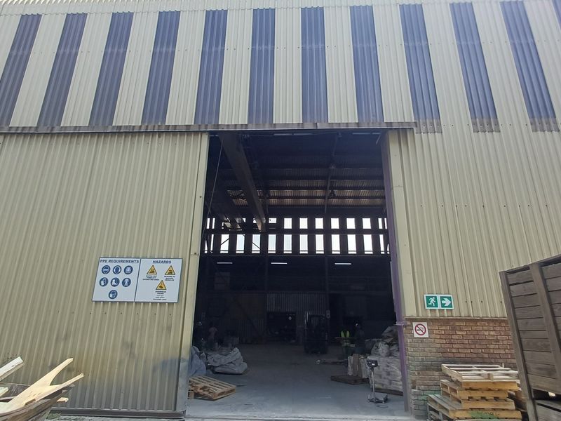 Industrial warehouse exterior featuring corrugated metal cladding, a large sliding access door, and visible overhead crane infrastructure.