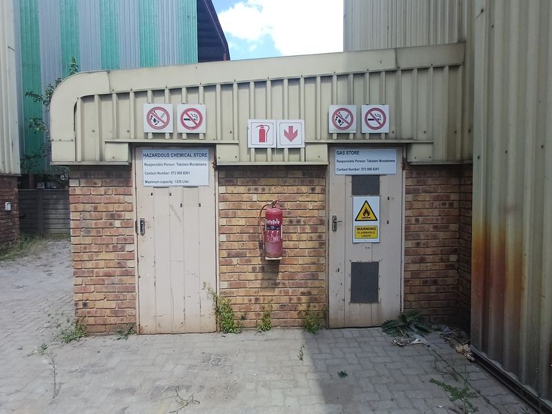 Industrial utility area featuring dedicated hazardous chemical and gas storage units with safety signage and fire suppression equipment.