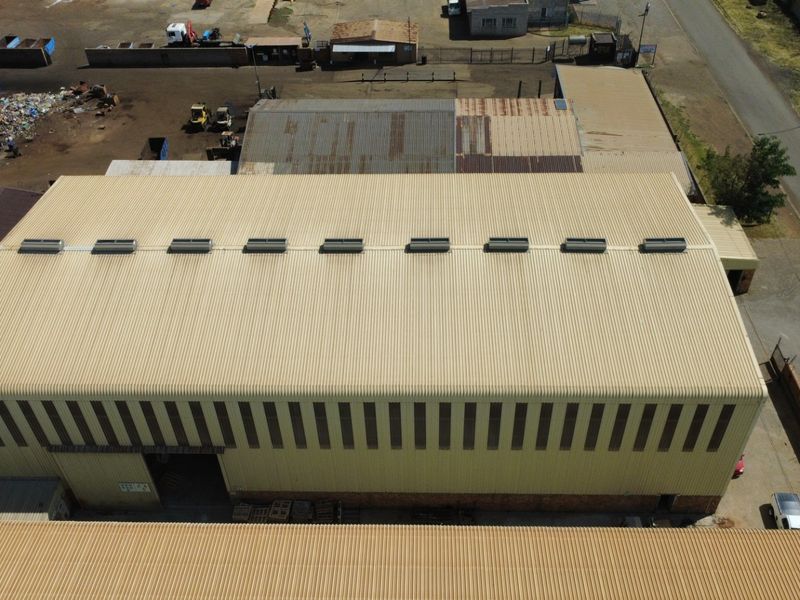 Aerial view of an industrial warehouse facility featuring a large corrugated metal roof with integrated skylights and side cladding.