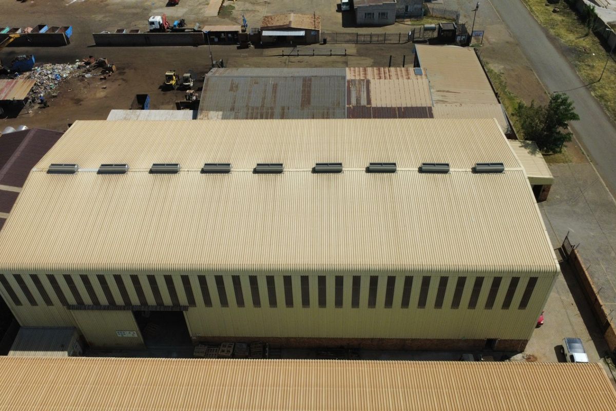 Aerial view of an industrial warehouse facility featuring a large corrugated metal roof with integrated skylights and side cladding.