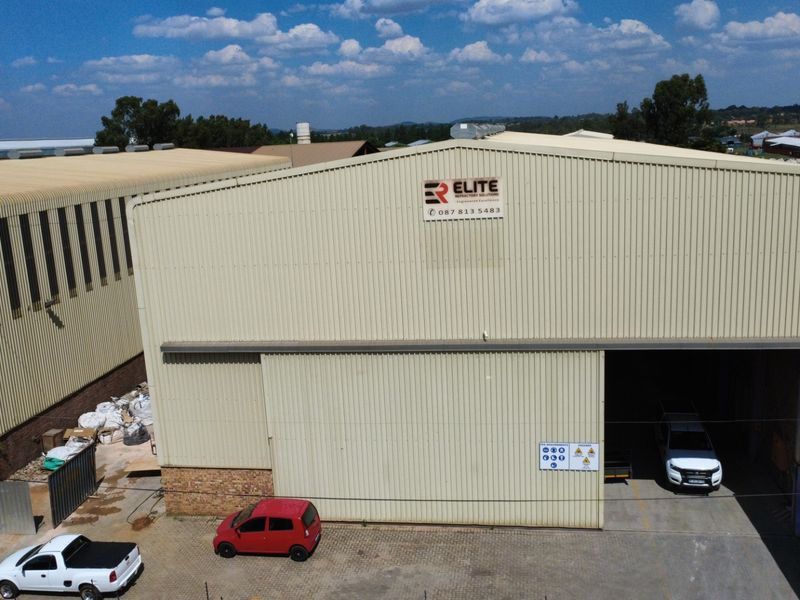 Aerial view of an industrial warehouse facility featuring corrugated metal cladding, a large sliding entrance door, and a paved yard area.