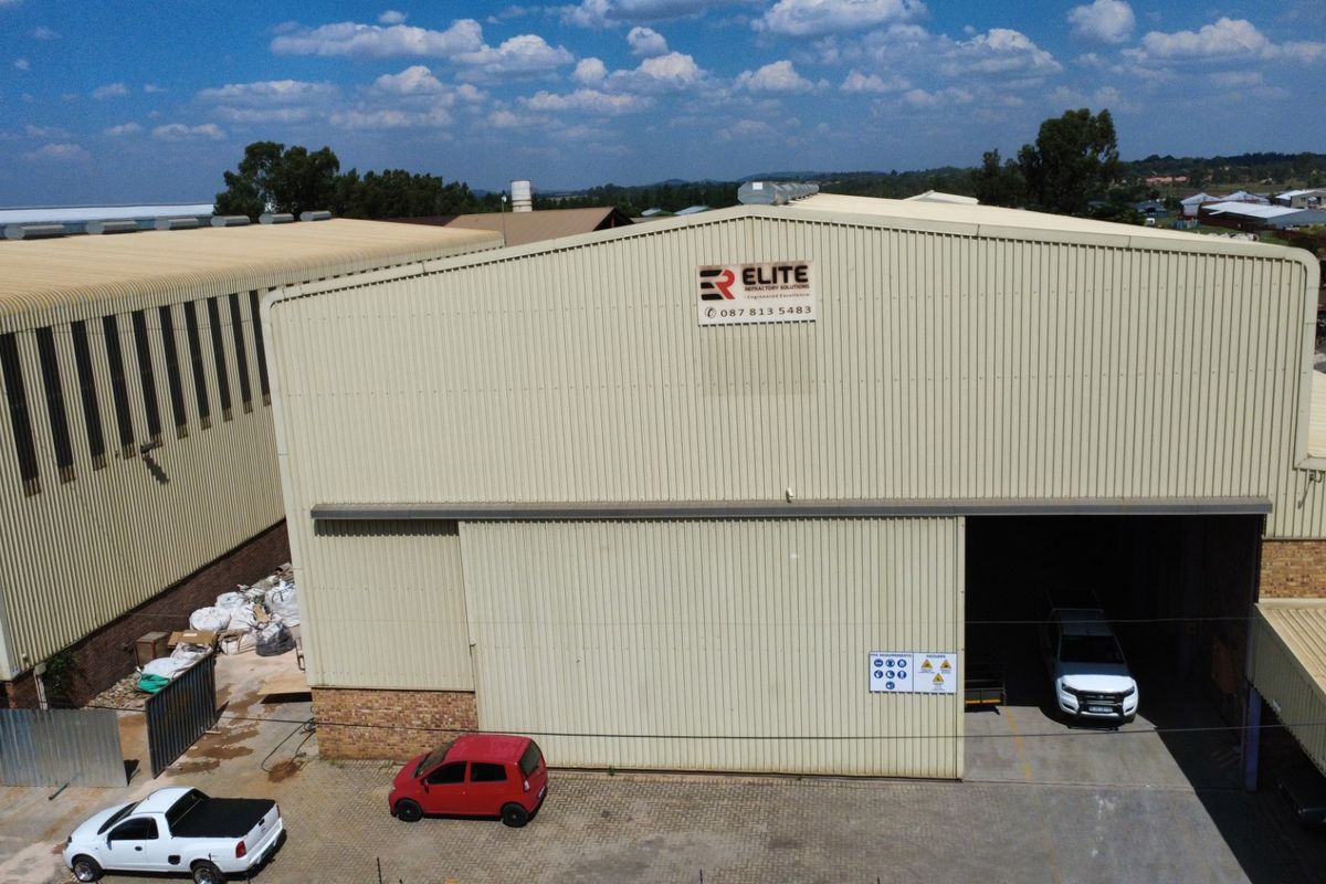 Aerial view of an industrial warehouse facility featuring corrugated metal cladding, a large sliding entrance door, and a paved yard area.