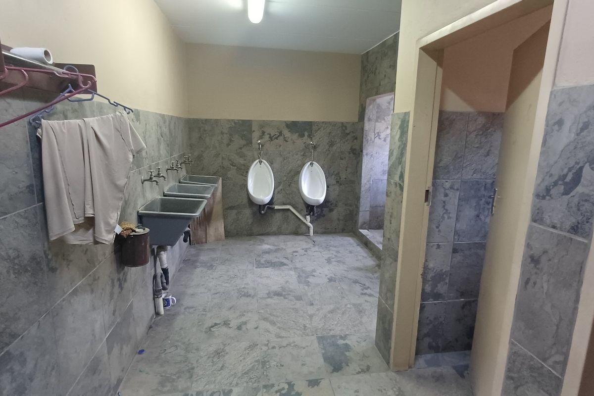 Industrial-style communal bathroom featuring wall-mounted urinals, multiple utility sinks, and full-height tiled wall finishes.