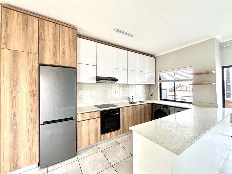 Modern kitchen featuring wood-grain and white cabinetry, stone countertops, integrated appliances, and tiled flooring with ample natural light.