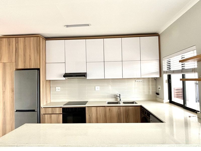 Modern kitchen featuring sleek white and wood-grain cabinetry, stone countertops, integrated appliances, and a tiled backsplash with ample storage space.