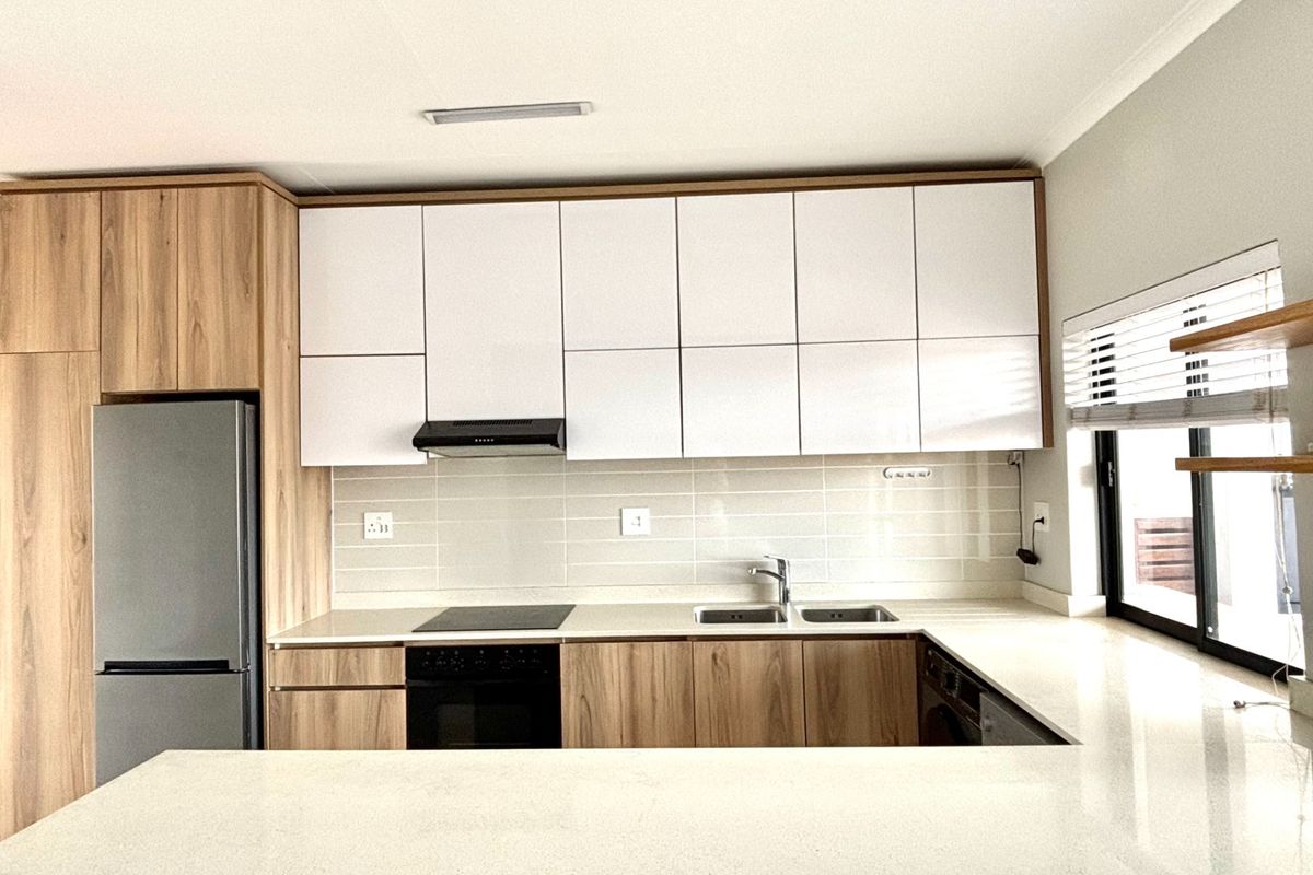 Modern kitchen featuring sleek white and wood-grain cabinetry, stone countertops, integrated appliances, and a tiled backsplash with ample storage space.
