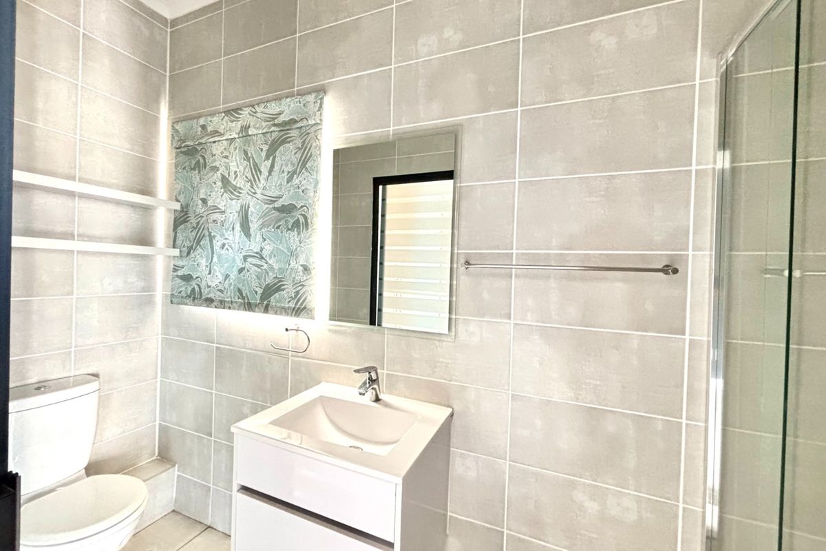 Modern bathroom featuring neutral wall tiles, a sleek vanity with basin, a glass-enclosed shower, and a contemporary toilet.
