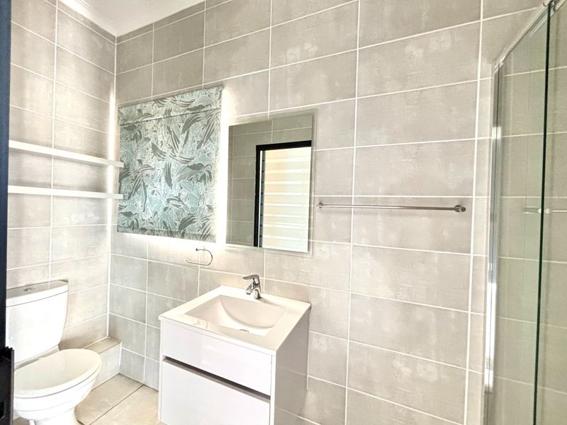 Modern bathroom featuring neutral wall tiles, a sleek vanity with basin, a glass-enclosed shower, and a contemporary toilet.