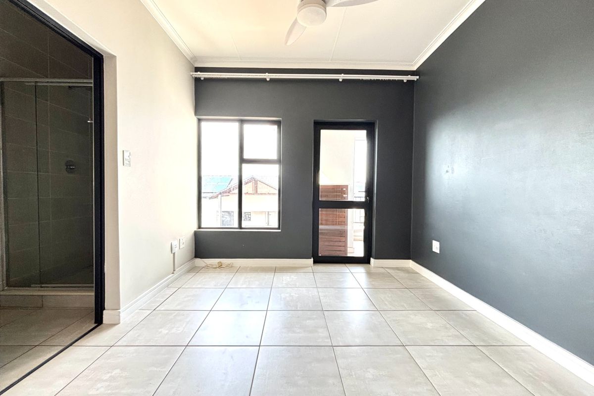 A bright, empty bedroom featuring neutral tiled flooring, a ceiling fan, and a modern dark accent wall with direct access to an outdoor area.