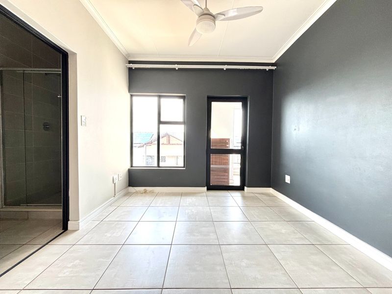 A bright, empty bedroom featuring neutral tiled flooring, a ceiling fan, and a modern dark accent wall with direct access to an outdoor area.