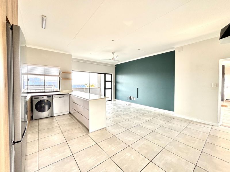 Spacious open-plan living and kitchen area featuring tiled flooring, a central island, and a feature wall, leading out to a balcony.