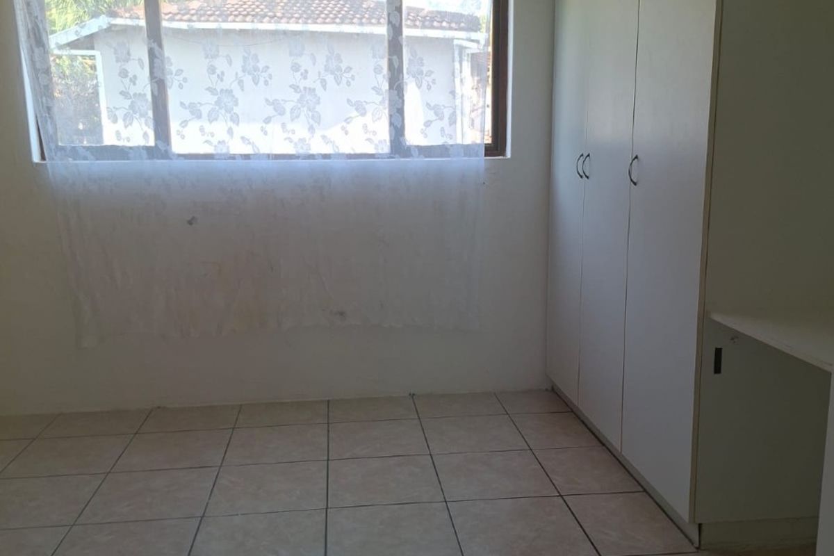 A bright, empty bedroom featuring neutral tiled flooring and ample built-in cupboard storage space.